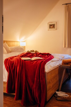 Een net opgemaakt bed met een rode deken, een houten hoofdbord, een bedlampje en een ingelijst foto op de muur.