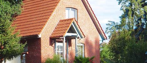 A red brick house with a sloped roof, a small porch, and a garden with various plants and a white spherical object.