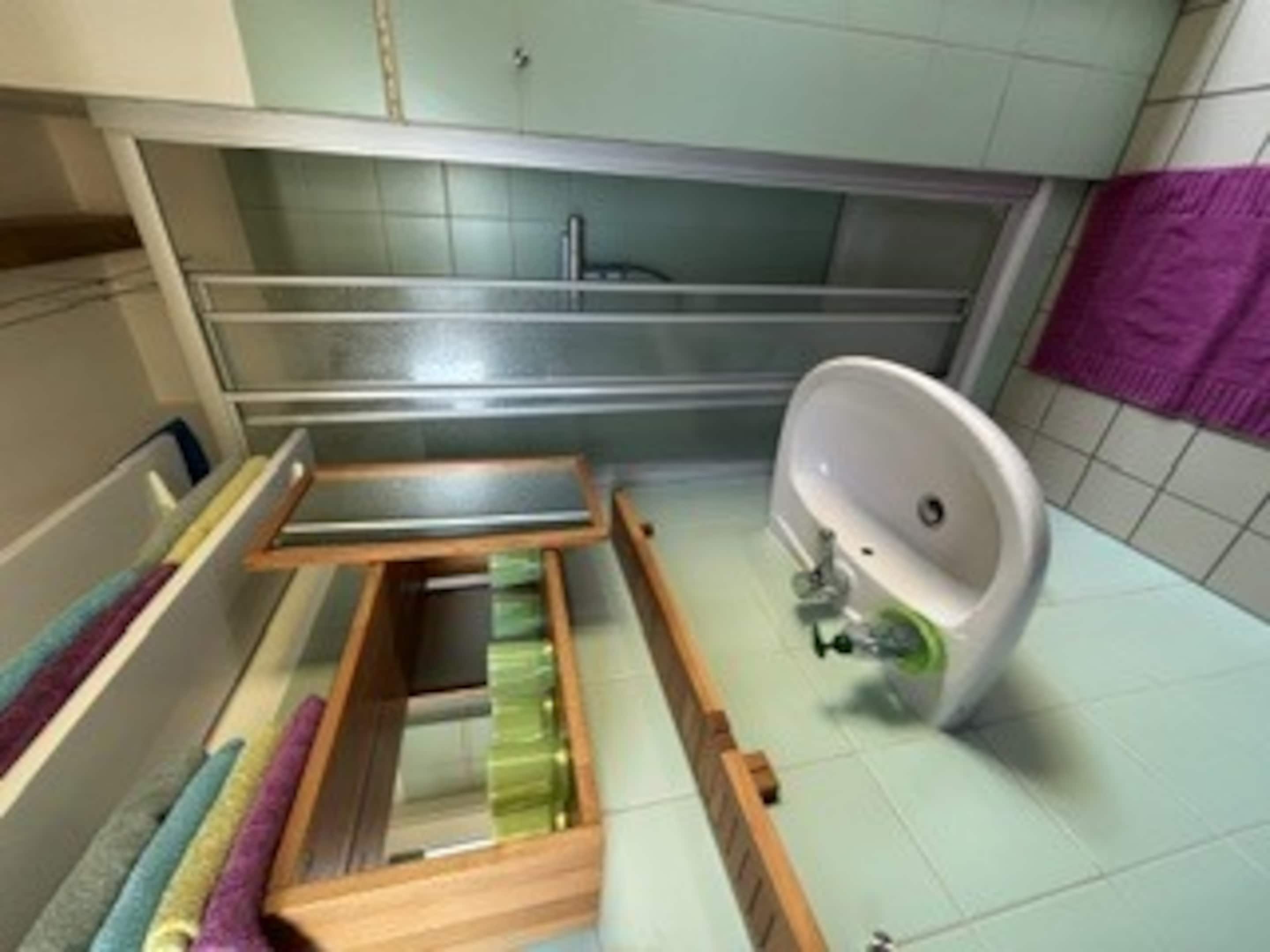 A bathroom with a built-in wooden shelf, a white sink, and a purple towel.