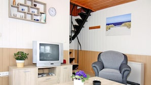 Een woonkamer met een televisie, een grijze fauteuil, een houten salontafel en een potplant.