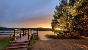 A wooden pier leading to a sandy beach with a lake and trees in the background. - Doppelhaushalften im Naturresort Drewitz (Nossentiner Huette)