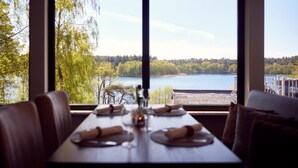 A dining table set with plates, cutlery, and a vase, overlooking a lake and forest. - Doppelhaushalften im Naturresort Drewitz (Nossentiner Huette)