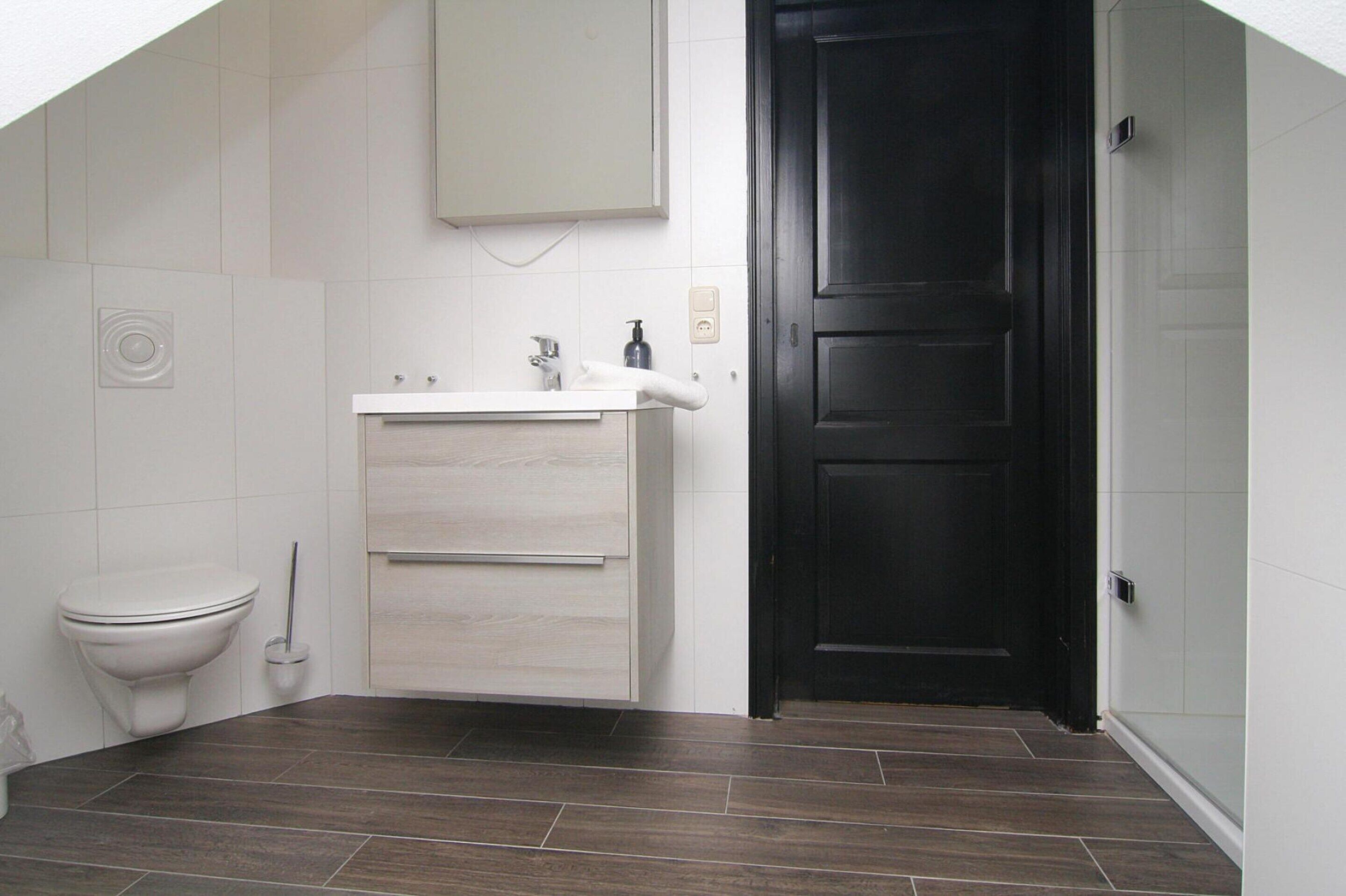 Ein Badezimmer mit Toilette, Waschbecken, Schrank und dunklem Holzboden.