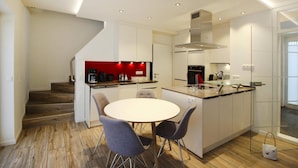 A modern kitchen with a central island, white cabinetry, and a red accent wall. - Doppelhaushalfte, St. Peter-ording (St. Peter-Ording)