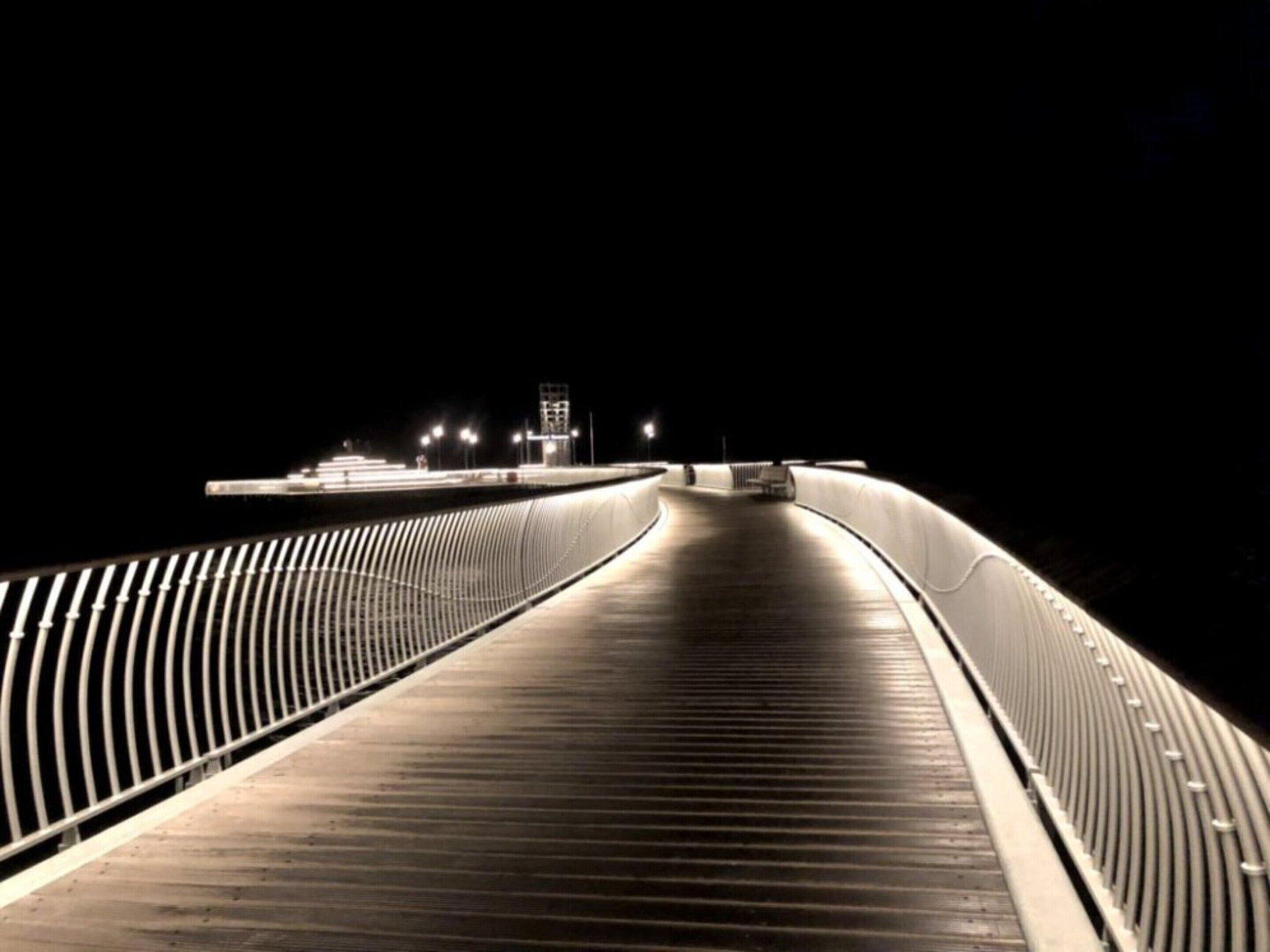 Una vista notturna di un ponte con una passerella arcuata e ringhiere.