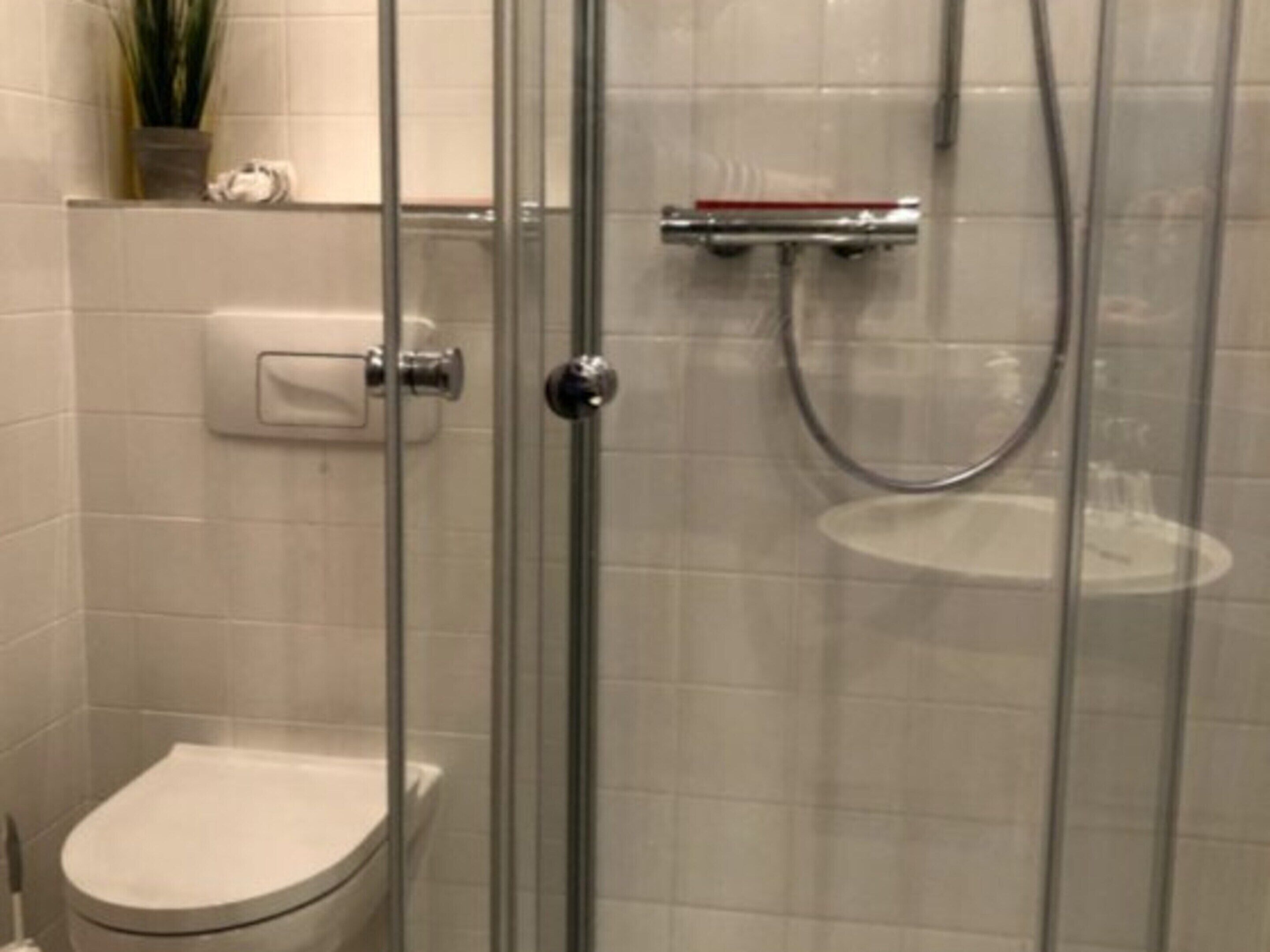 A glass-enclosed shower stall with a handheld showerhead and a wall-mounted faucet.