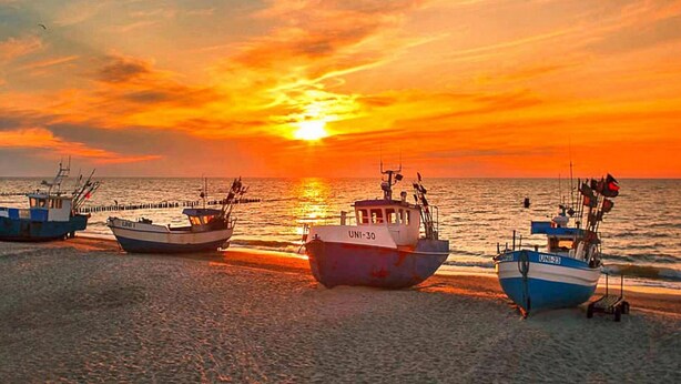 A sunset over a beach with several boats anchored. - Villa in Mielno Near Seaside Beach (Mielno)
