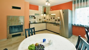 A modern kitchen with a dining area, featuring a stainless steel refrigerator, a built-in oven, and a round dining table with chairs. - Villa in Mielno Near Seaside Beach (Mielno)