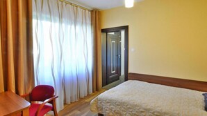 A hotel room with a wooden floor, a bed with a patterned duvet, a wooden desk, a red chair, and a window with sheer curtains. - Villa in Mielno Near Seaside Beach (Mielno)