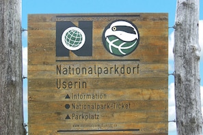 Et træskilt med teksten "Nationalparkdorf Userin" og ikoner for information, billetter og parkeringsplads.