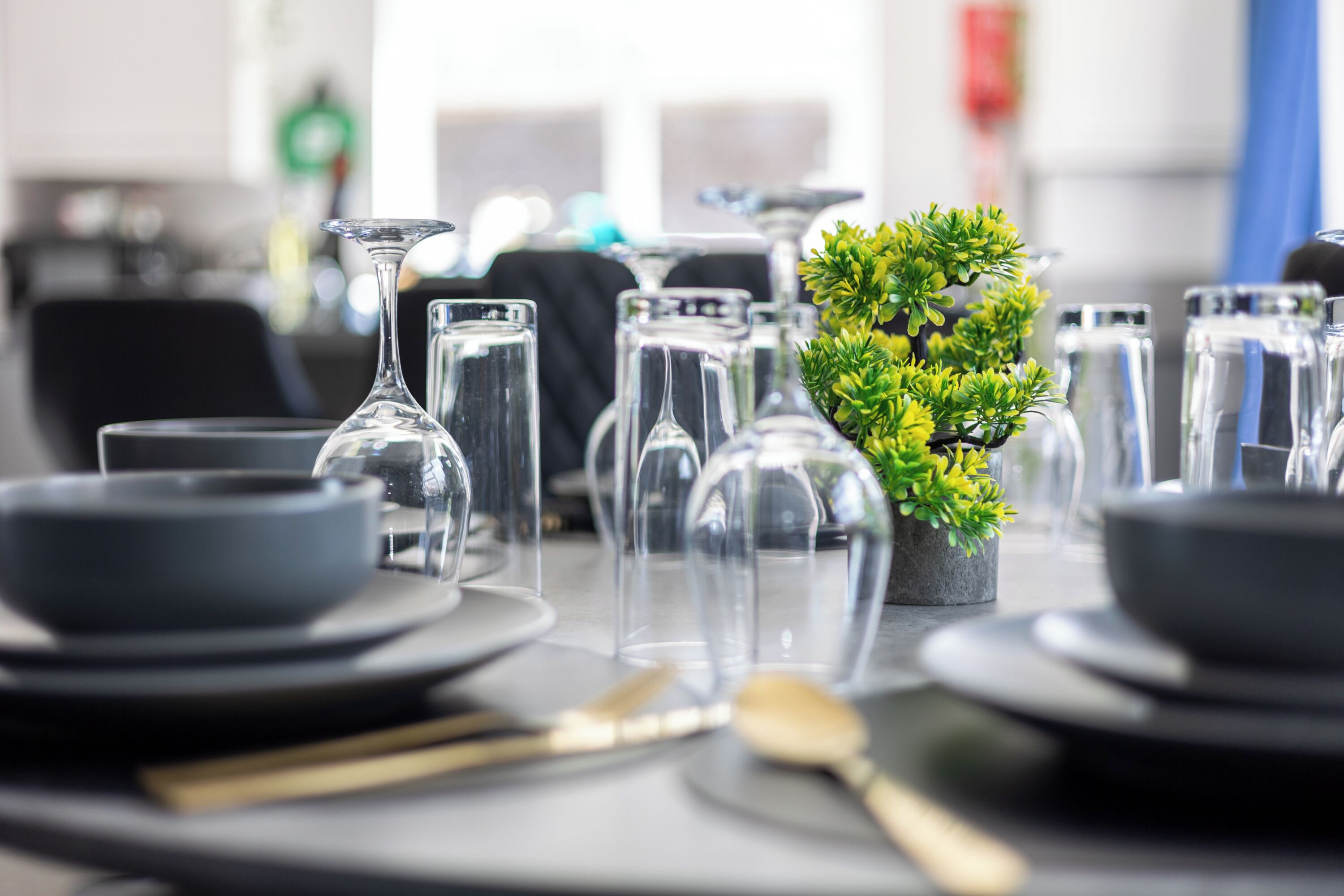 Una mesa dispuesta con cristalería transparente, cuencos negros y una pequeña planta en maceta.