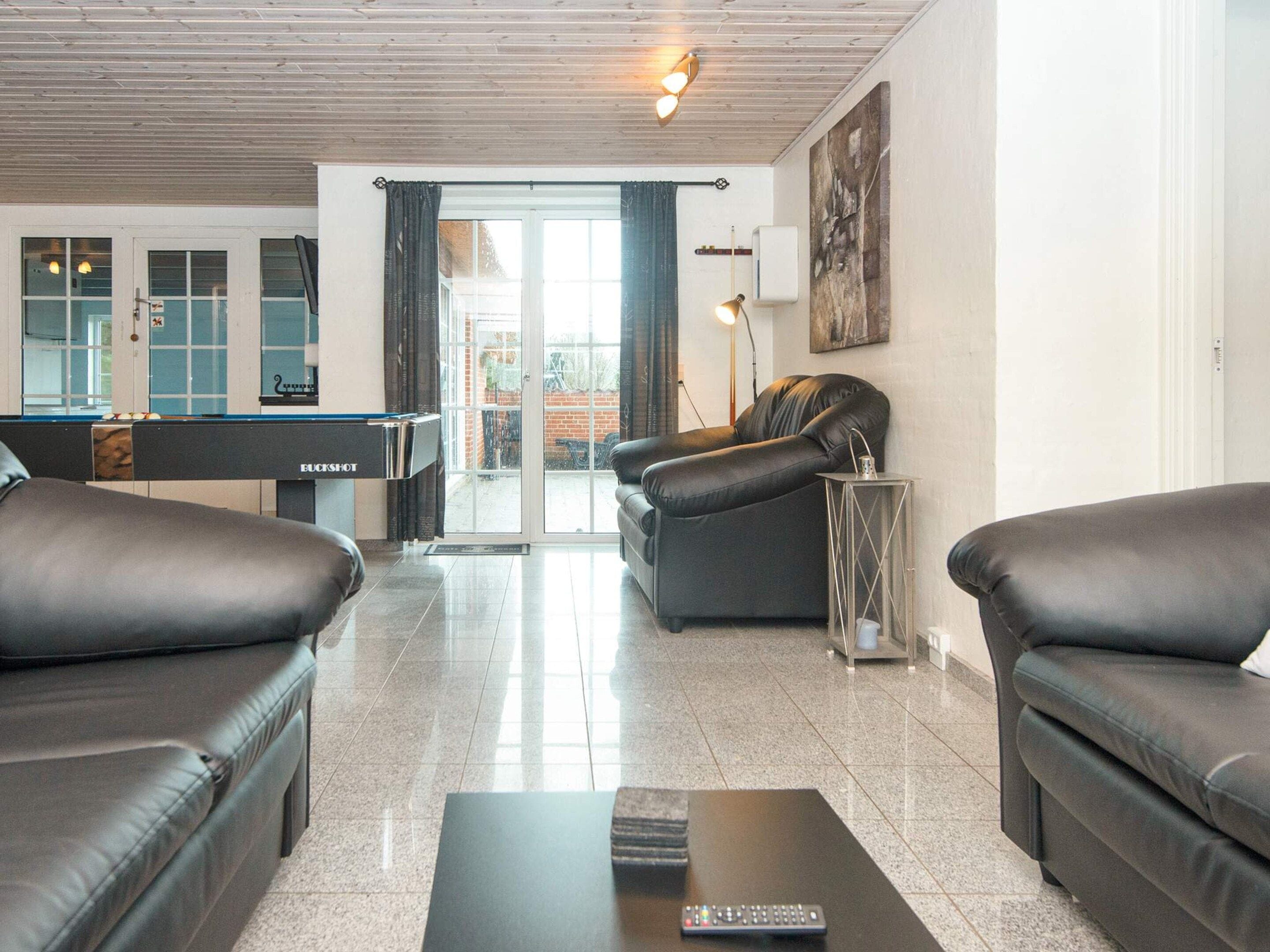 A modern living room with a pool table, leather sofas, and a billiards cue rack.
