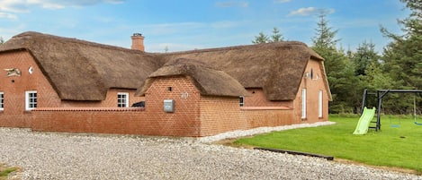 A brick house with a thatched roof, a number '20' sign, and a green slide in the yard.
