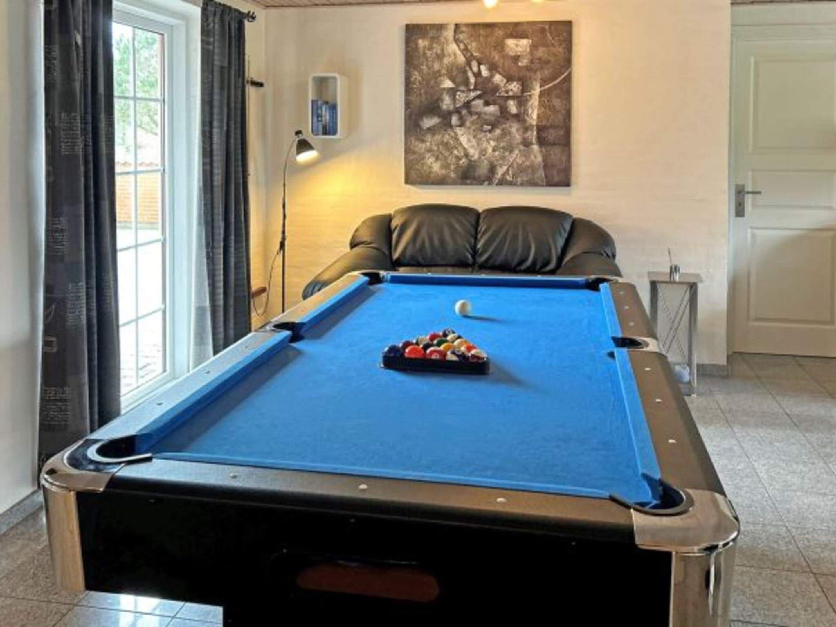 Une table de billard avec une boule blanche et des billes éparpillées, une lampe et un tableau accroché au mur.