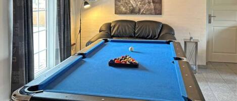 Une table de billard avec une boule blanche et des billes éparpillées, une lampe et un tableau accroché au mur.