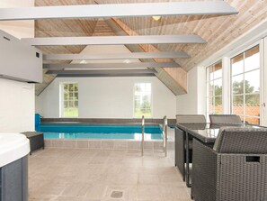 A modern indoor pool area with a clear view of the pool, a seating area with wicker furniture, and large windows allowing natural light. - 4 Star Holiday Home in Ulfborg (Ulfborg)