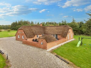 A brick house with a thatched roof, a gravel driveway, and a green lawn.
