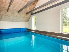 En inomhuspool med ett tak av trä och en blå bänk.
