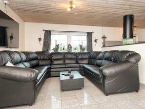 A living room with a large L-shaped leather sofa, a small coffee table, and a window with curtains. - 4 Star Holiday Home in Ulfborg (Ulfborg)