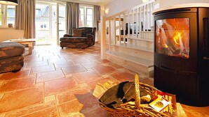 Un salon chaleureux avec une cheminée, un panier en osier rempli de bûches et un canapé.