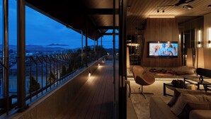 Una sala de estar moderna con un televisor grande, asientos cómodos y un balcón con vistas a la ciudad y a las montañas.