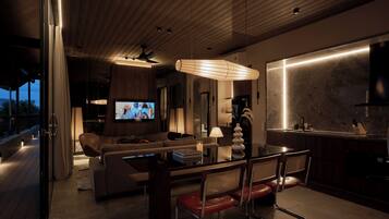 A modern living room with a sofa, a dining table, and chairs. There is a television, a lamp, and a kitchen area with a marble countertop.