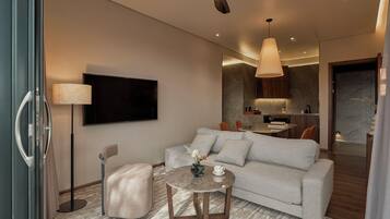 A modern living room with a grey sofa, a round coffee table, a floor lamp, and a flat-screen TV mounted on the wall.
