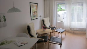 Et moderne værelse med et hvidt bord, to stole, et lille rundt bord med en vase, en radiator og et vindue med gardiner.