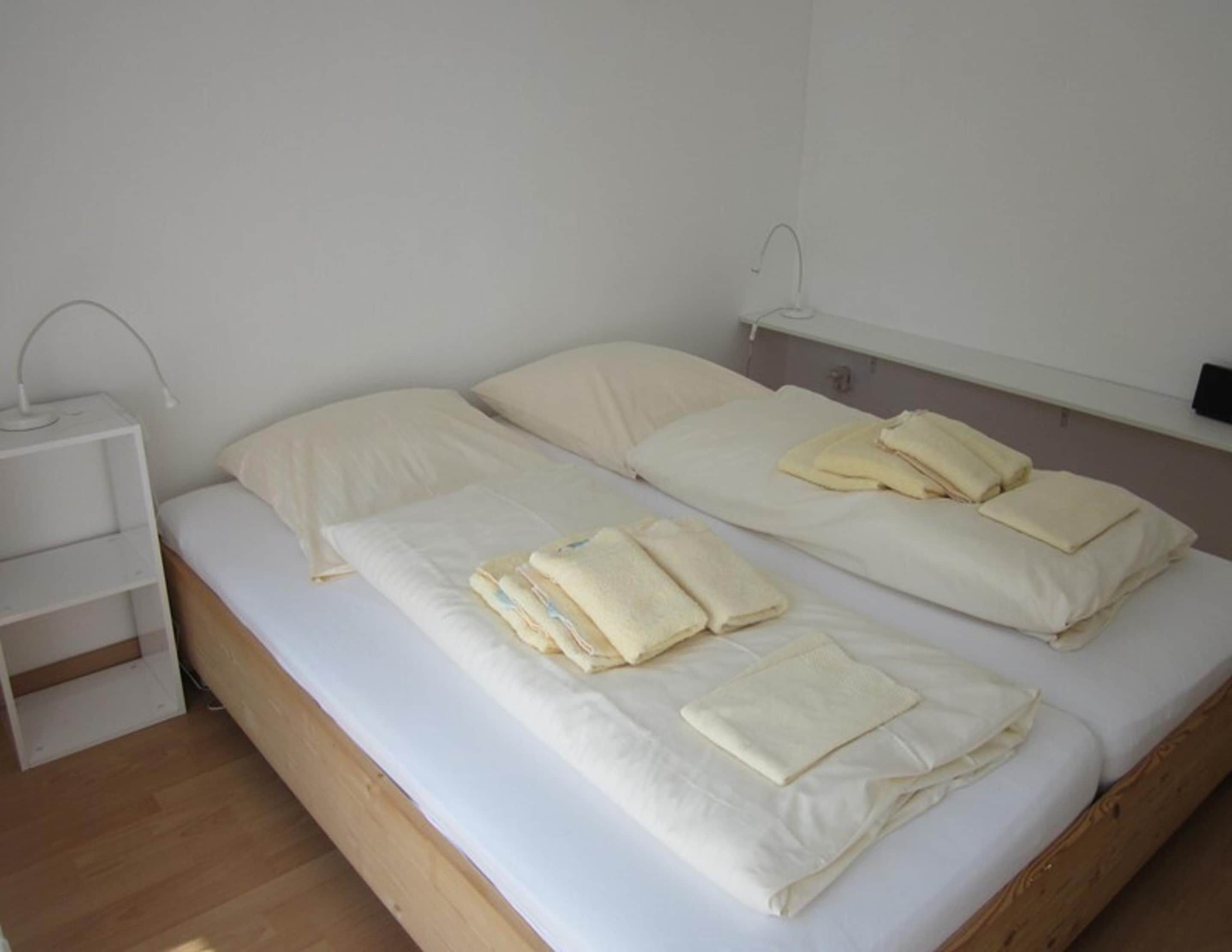 Ein Doppelbett mit zwei Kissen und gefalteten Handtüchern, ein Nachttisch mit Lampe und ein Holzboden.