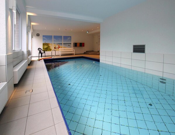 An indoor swimming pool with tiled walls and a bench near the window. - Ferienwohnung in Westerland auf Sylt (Sylt)