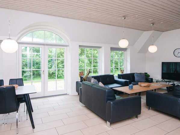 A spacious living area with a large window, a sofa set, a dining table, and a television.