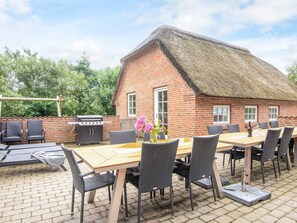 A brick building with a thatched roof, outdoor seating with tables and chairs, and a grill. - 4 Star Holiday Home in Ulfborg (Ulfborg)