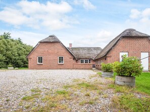 Ein Backsteinhaus mit einem Strohdach, einer Schotterauffahrt und einem kleinen Garten mit einem Blumentopf.