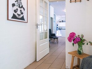 Ein Flur mit einer Tür zu einem Zimmer, einem Sessel und einem Tisch mit Blumen.