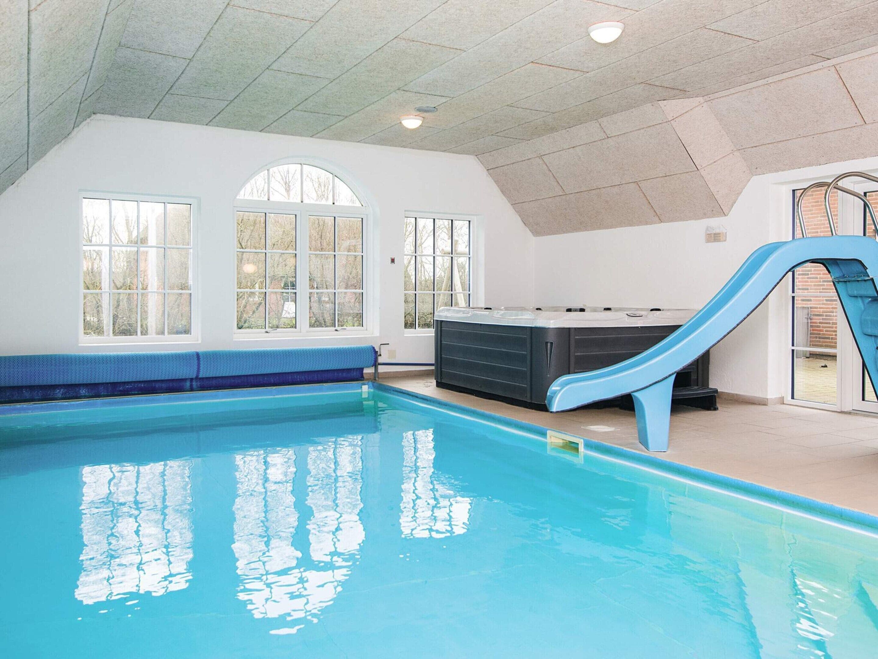 An indoor swimming pool with a blue slide, large windows, and a sauna area.