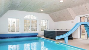 En inomhuspool med en blå vattenrutschkana, stora fönster och en bastu.