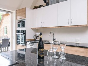 A modern kitchen with white cabinets, a built-in oven, a coffee maker, and a bottle of champagne on the counter. - 4 Star Holiday Home in Ulfborg (Ulfborg)
