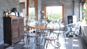 Un comedor con mesa de madera y sillas metálicas, un armario con botellas y un ventanal con vistas a zonas verdes.