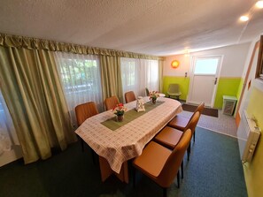 Comedor con una mesa preparada para cuatro personas, sillas alrededor y una ventana con cortinas en un lateral.