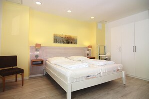 A bedroom with a bed, bedside tables, a chair, a wardrobe, and a wall-mounted artwork. - Ferienwohnung Grosser Seestern in Wiek (Wiek)
