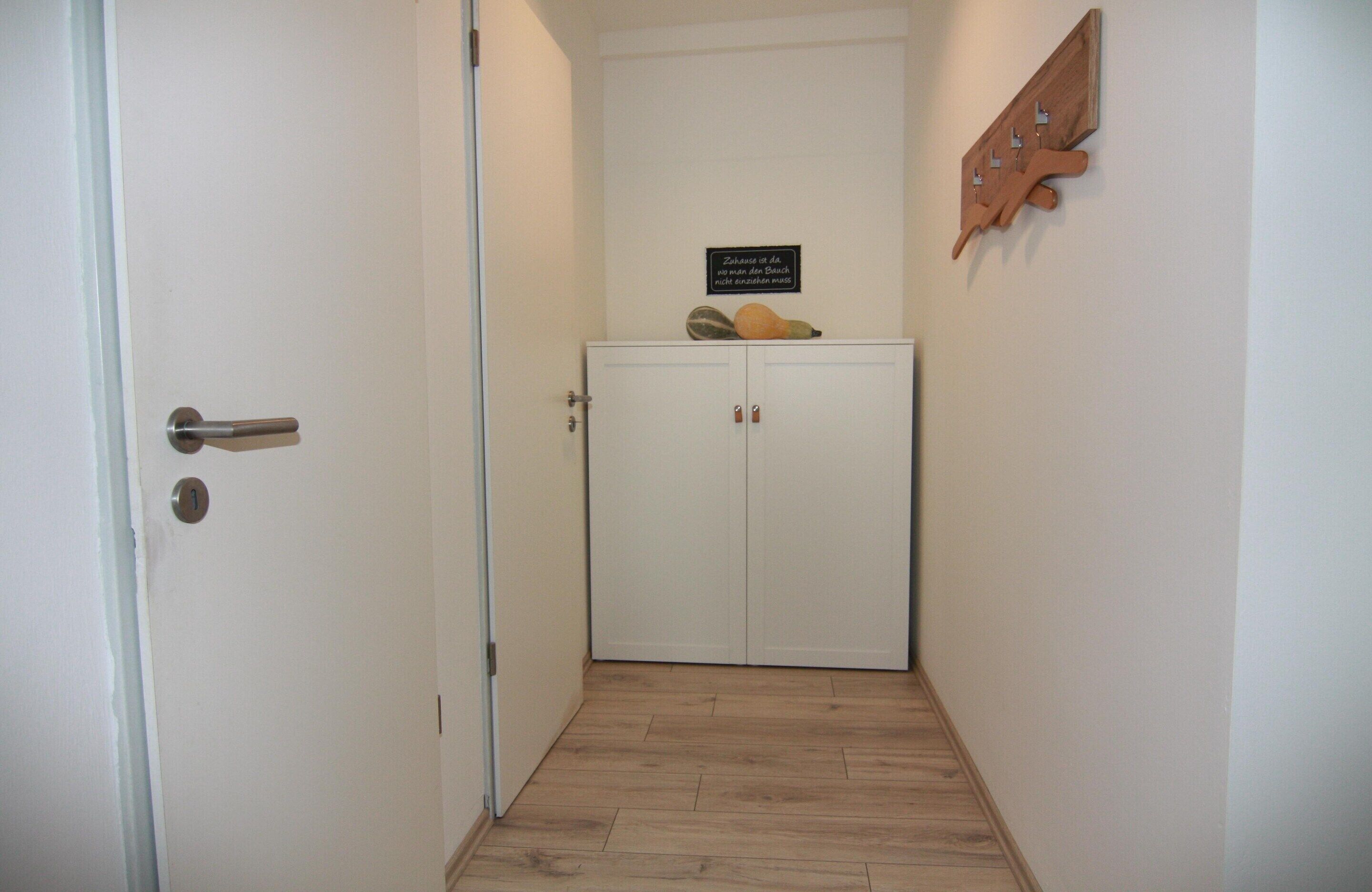 Un passadís estret amb una porta blanca, un paviment de fusta i un armari blanc de dues portes.