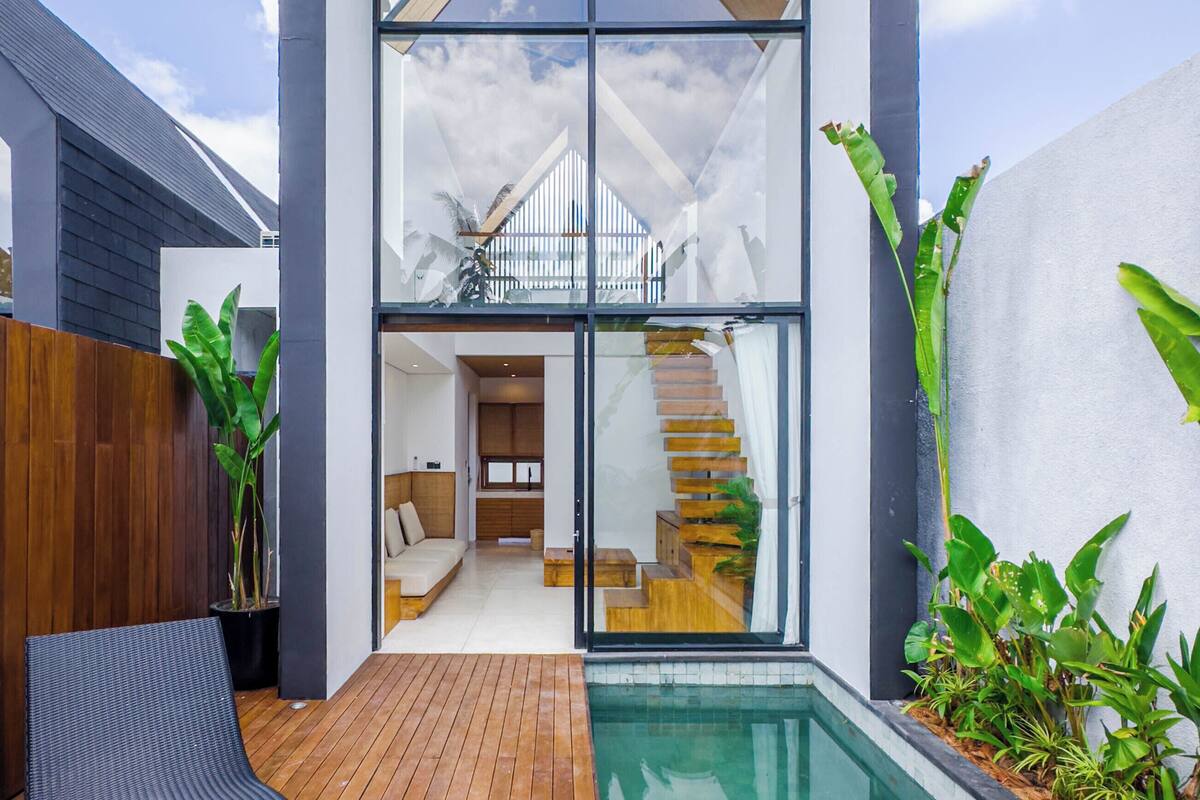 A modern house with a large glass facade, a wooden deck, and a swimming pool.