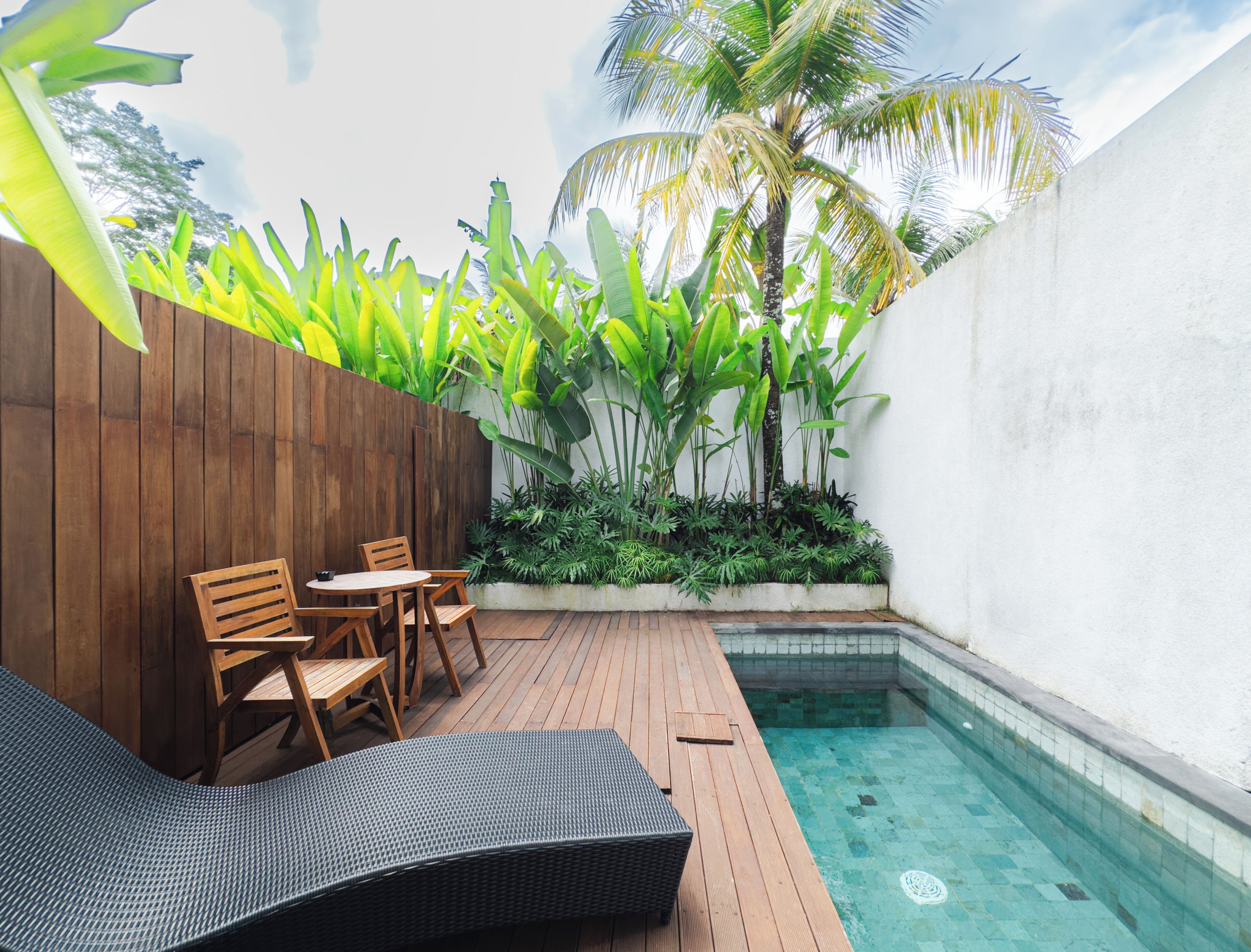 A wooden deck with a pool, surrounded by lush tropical plants and a wooden fence.