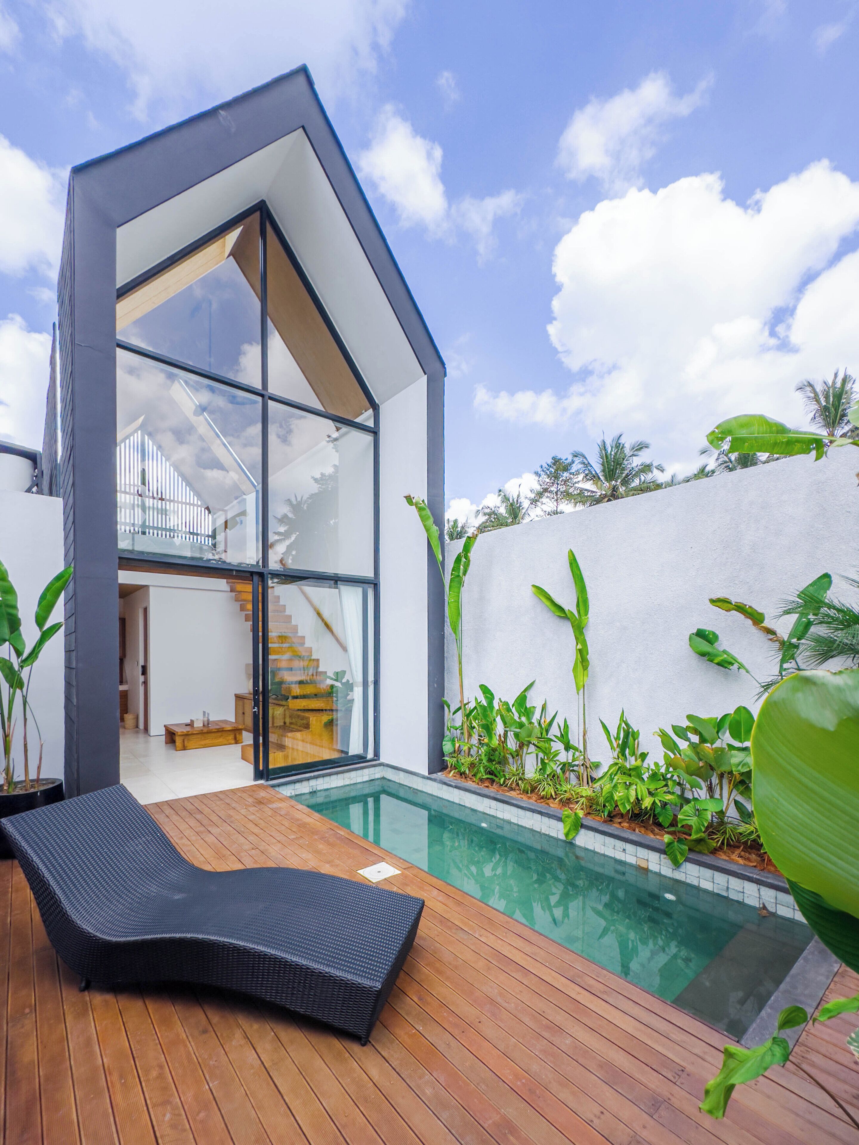 A modern house with a glass facade, a wooden deck, and a swimming pool.