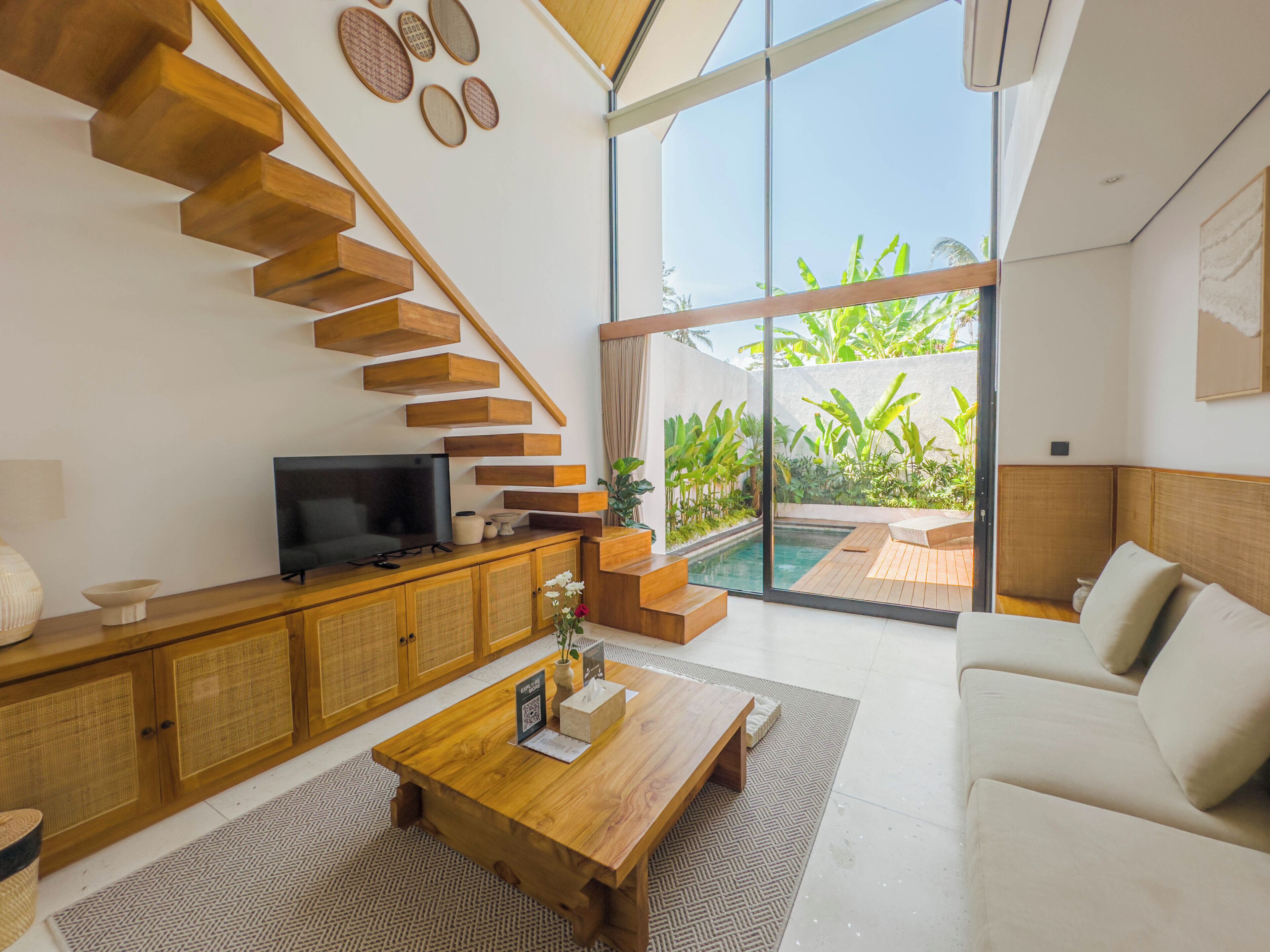 A modern living room with a wooden staircase, a flat-screen TV, a coffee table, and a sofa.