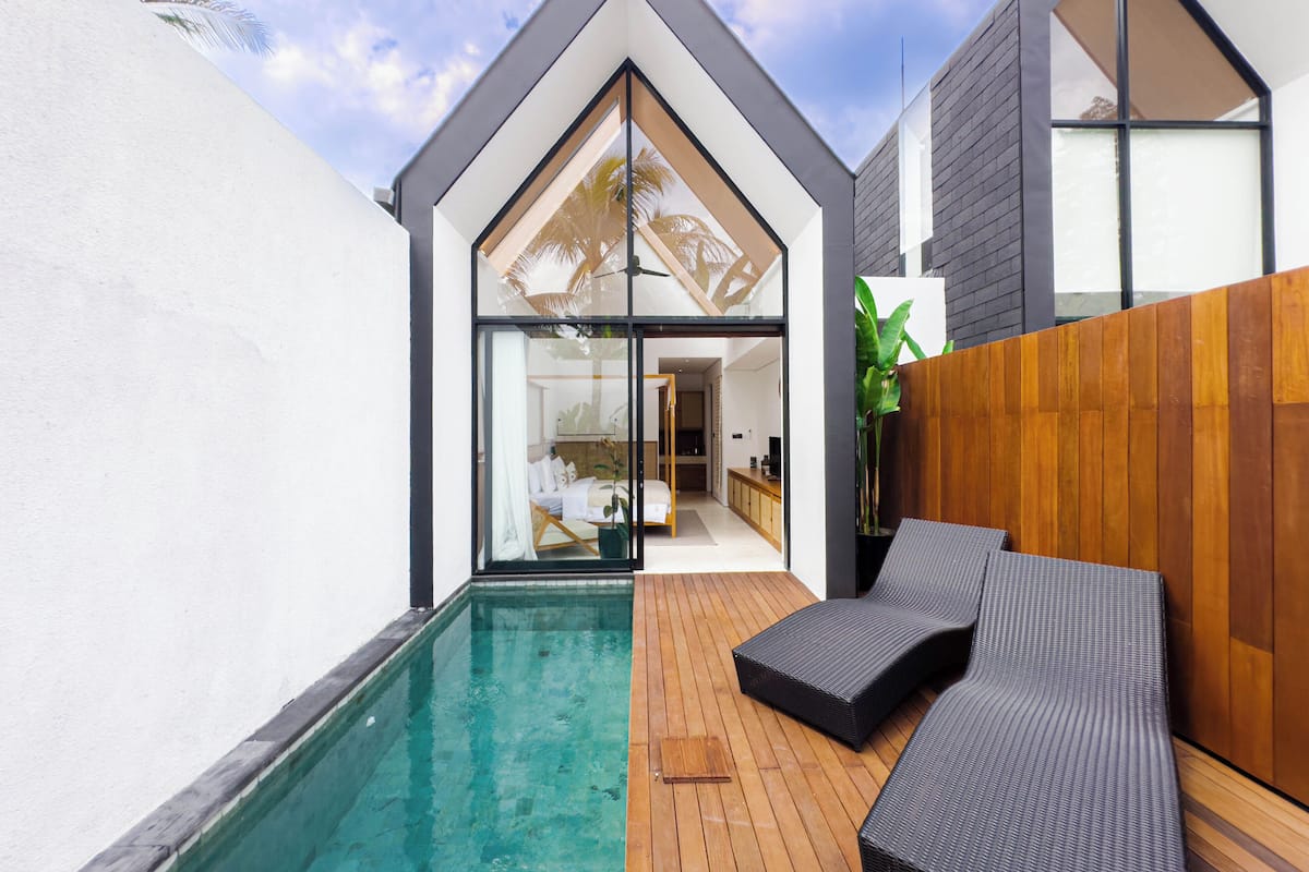 A modern house with a swimming pool, wooden deck, and a lounge area with a view of the interior.