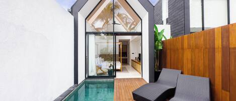 A modern house with a swimming pool, wooden deck, and a lounge area with a view of the interior.