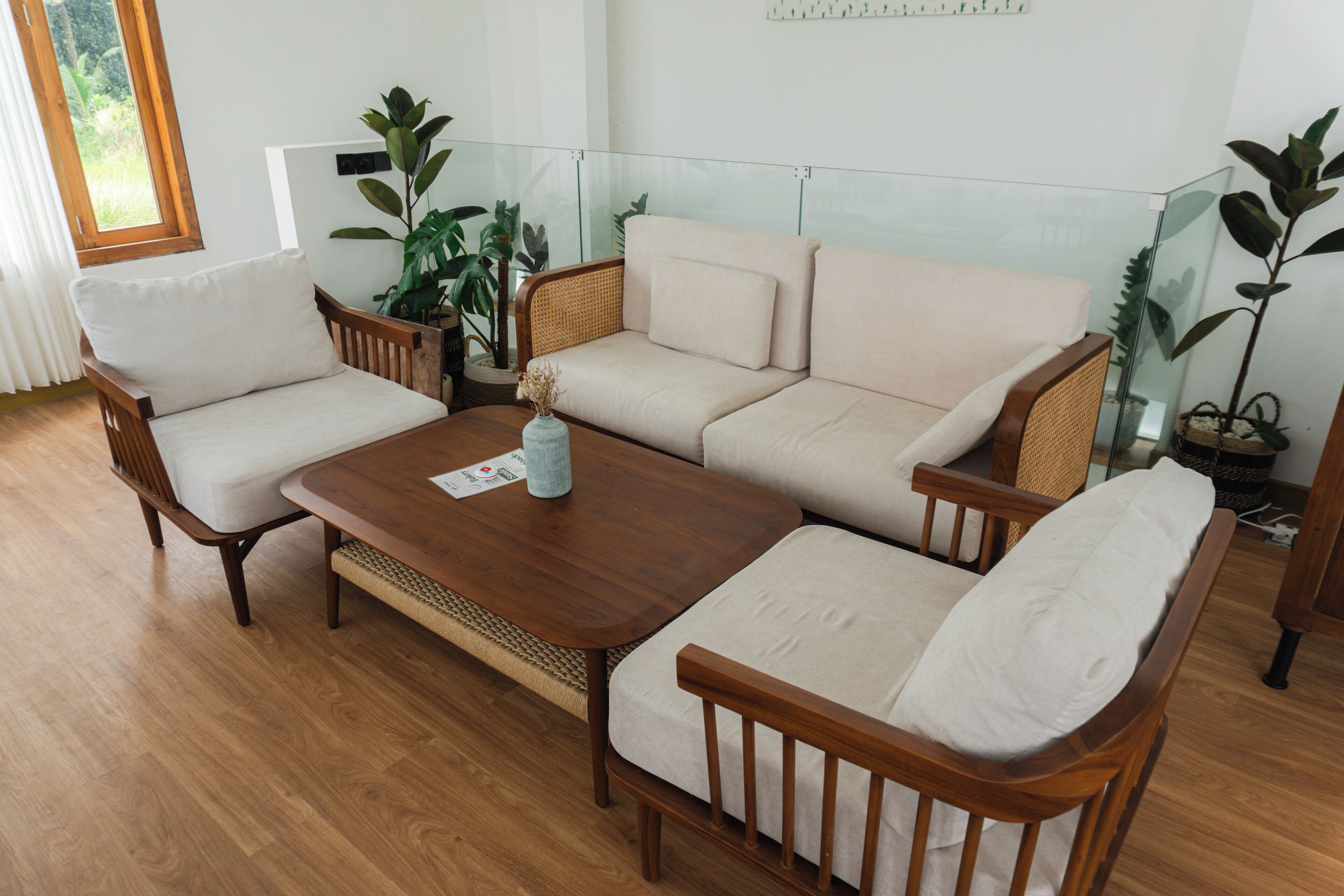 A living room with a wooden coffee table, two armchairs, a sofa, and several potted plants.
