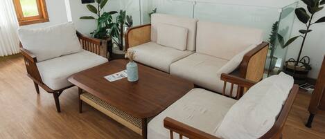 A living room with a wooden coffee table, two armchairs, a sofa, and several potted plants.
