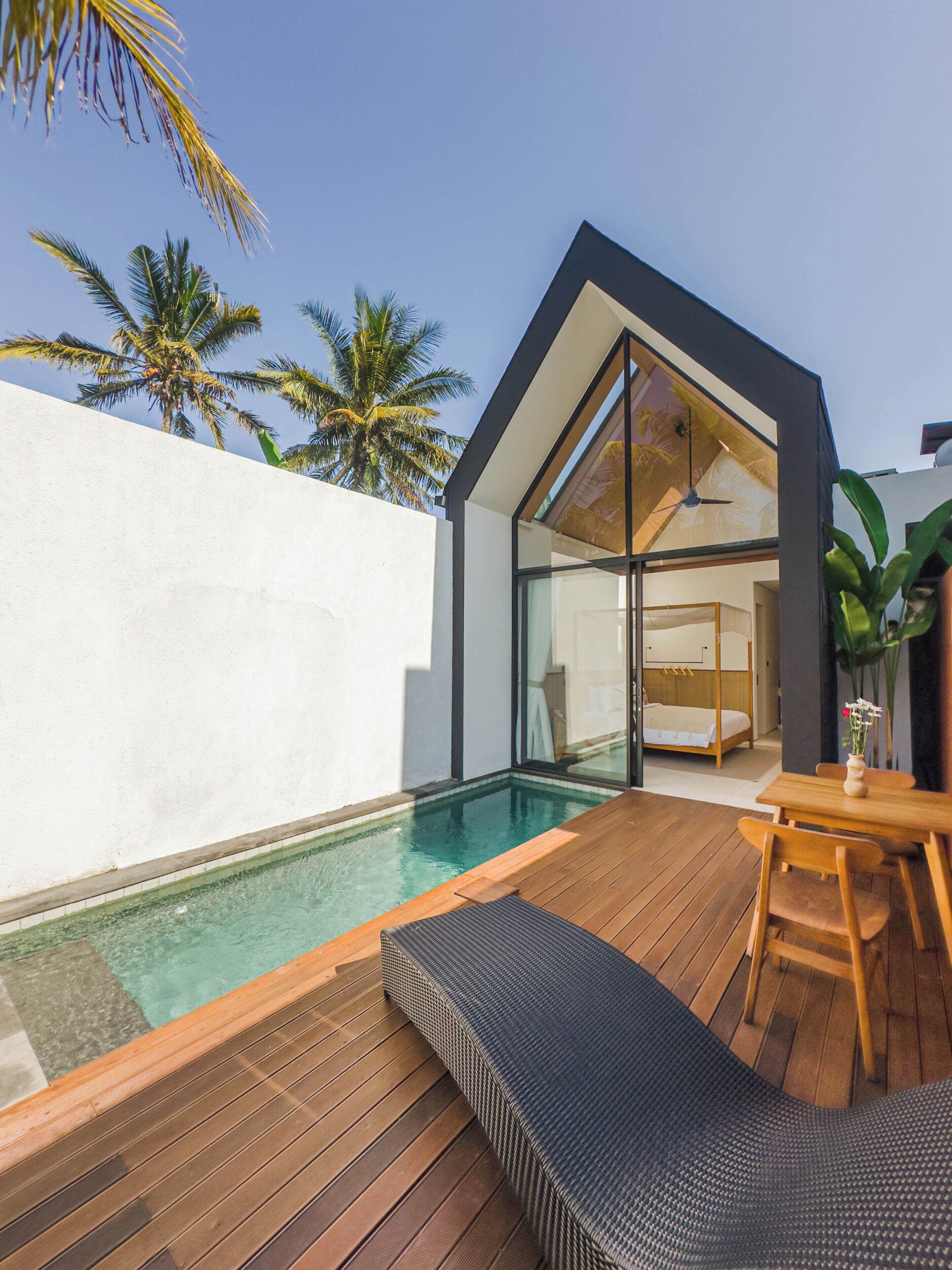 A modern villa with a swimming pool, wooden deck, and a large glass door leading to a bedroom.